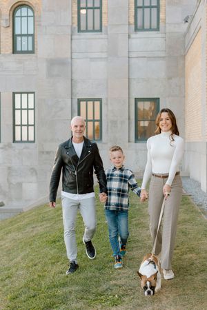 Family walking and playing together on a grassy hill slope outside a stone building in matching casual outfits.