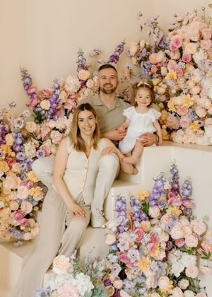 Beautiful floral family portrait setup with pink and purple flowers against beige backdrop on white couch.