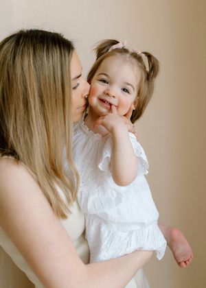 Sweet moment between parent and child wearing white outfits as they share a tender kiss and smile.