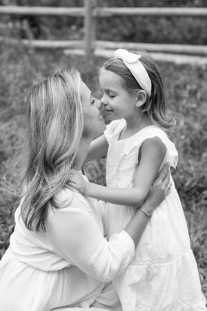 A tender black and white portrait series showing a mother and daughter in white dresses sharing loving moments outdoors.
