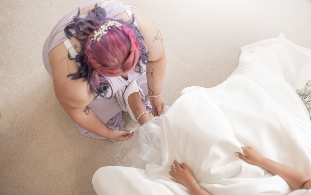 A person wearing colorful tattoos and pink hair is photographed from above while sitting next to white fabric the bride.