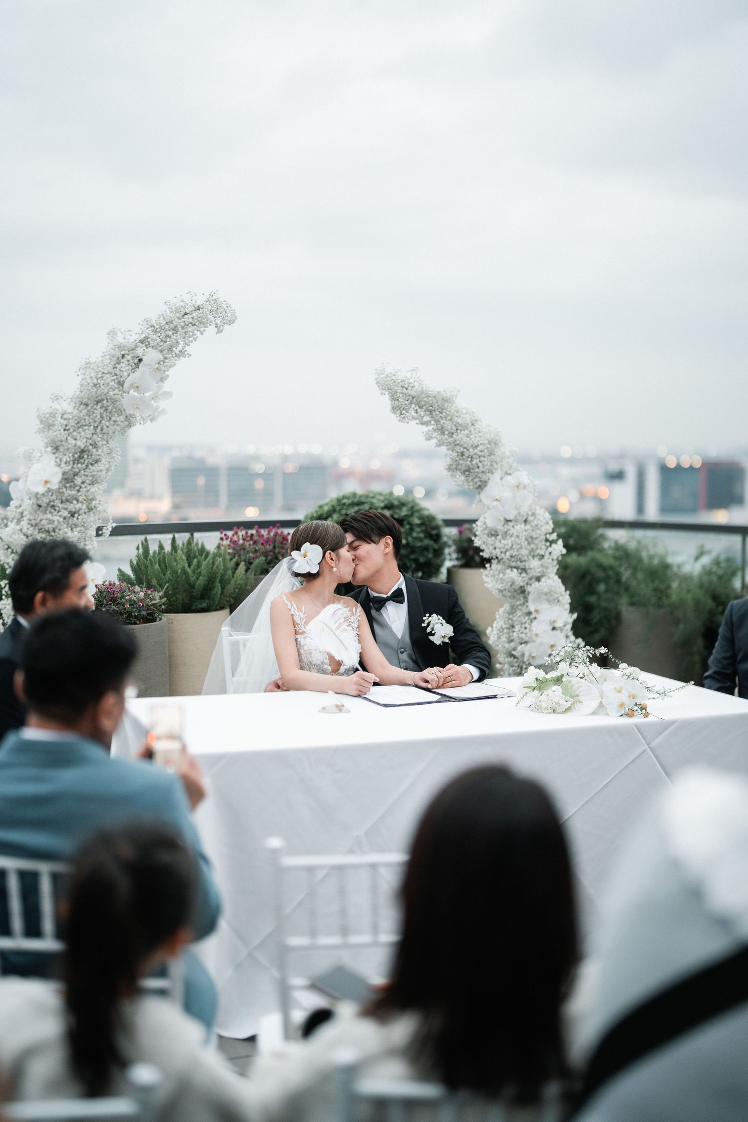 Rooftop wedding ceremony setup with white floral arches against a city skyline.