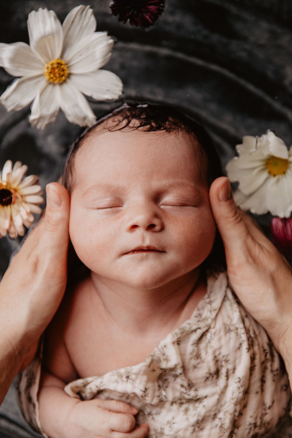 Un nouveau-né endormi dans un bain fleuri entouré de délicates fleurs de roses blanches repose doucement dans les mains.