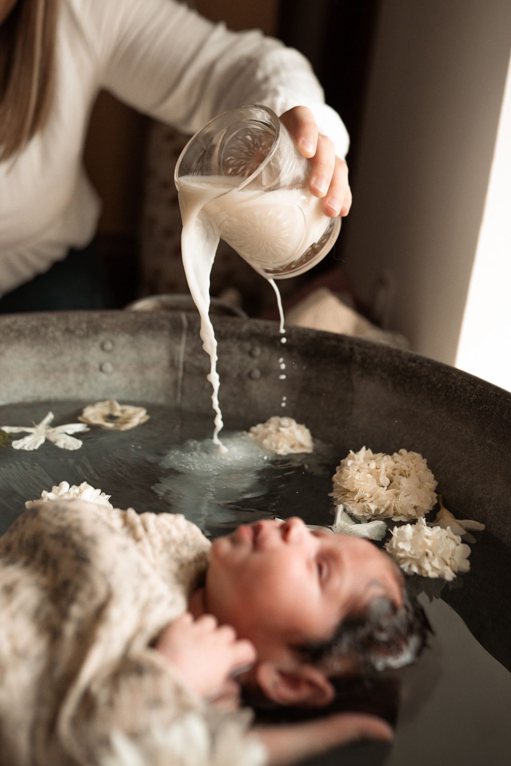 Un nouveau-né endormi dans un bain fleuri entouré de délicates fleurs de roses blanches repose doucement dans les mains.
ou on verse du lait
