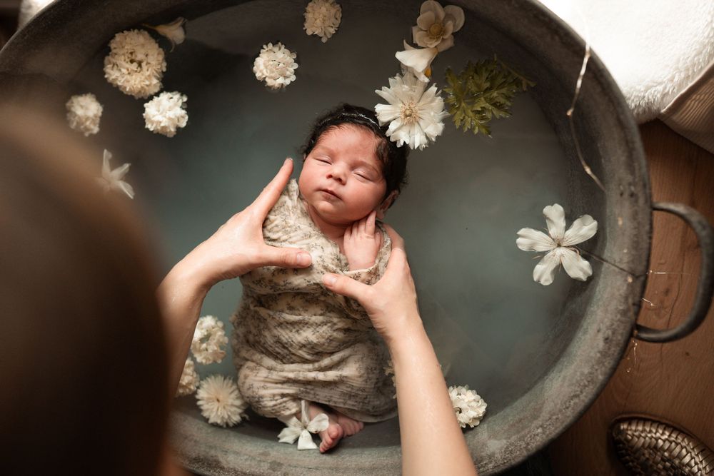 Un nouveau-né endormi dans un bain fleuri entouré de délicates fleurs de roses blanches repose doucement dans les mains.