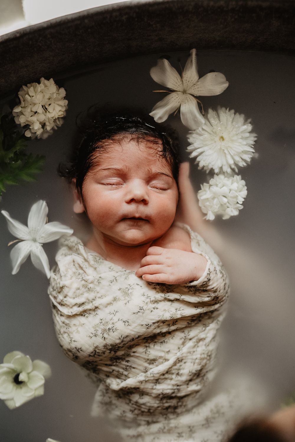 Un nouveau-né endormi dans un bain fleuri entouré de délicates fleurs de roses blanches repose doucement dans les mains.