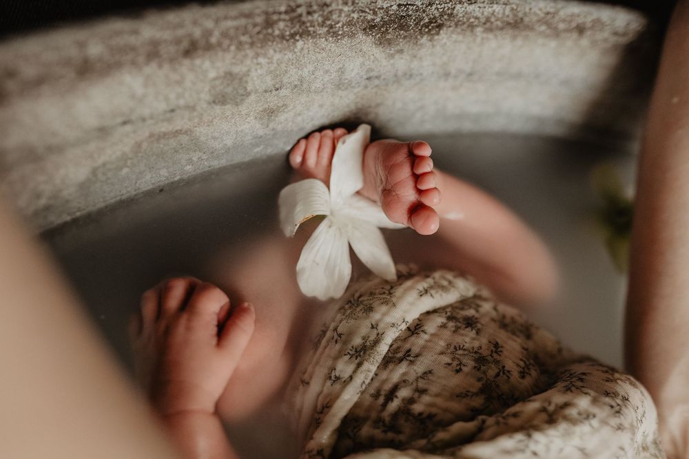 Un nouveau-né endormi dans un bain fleuri entouré de délicates fleurs de roses blanches repose doucement dans les mains.