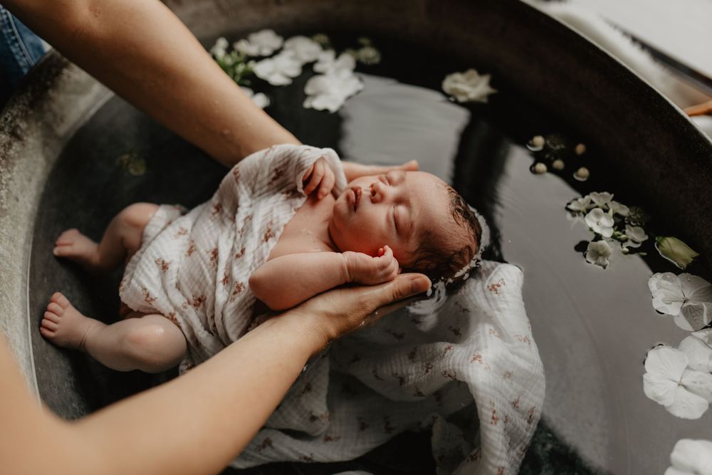 Un nouveau-né endormi dans un bain fleuri entouré de délicates fleurs de roses blanches repose doucement dans les mains.