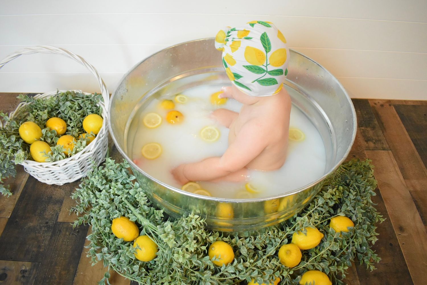 A citrus-themed bath setup with lemons and greenery surrounding a metal tub.