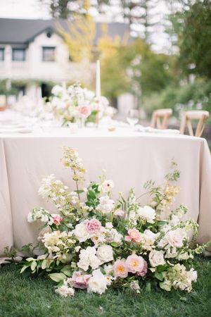 Delicate pink and white floral arrangements with greenery line a low white wall in an outdoor garden setting. MacArthur Place Hotel