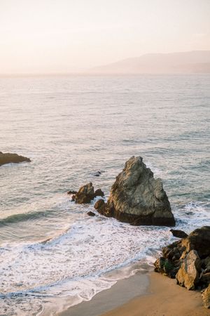 Scenic coastal landscape with rocky outcrops and crashing waves along a misty California beach at sunset. San Francisco engagement session.
