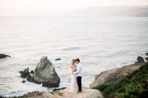 A romantic coastal photoshoot with misty waves crashing against rocky cliffs at sunset. San Francisco, CA