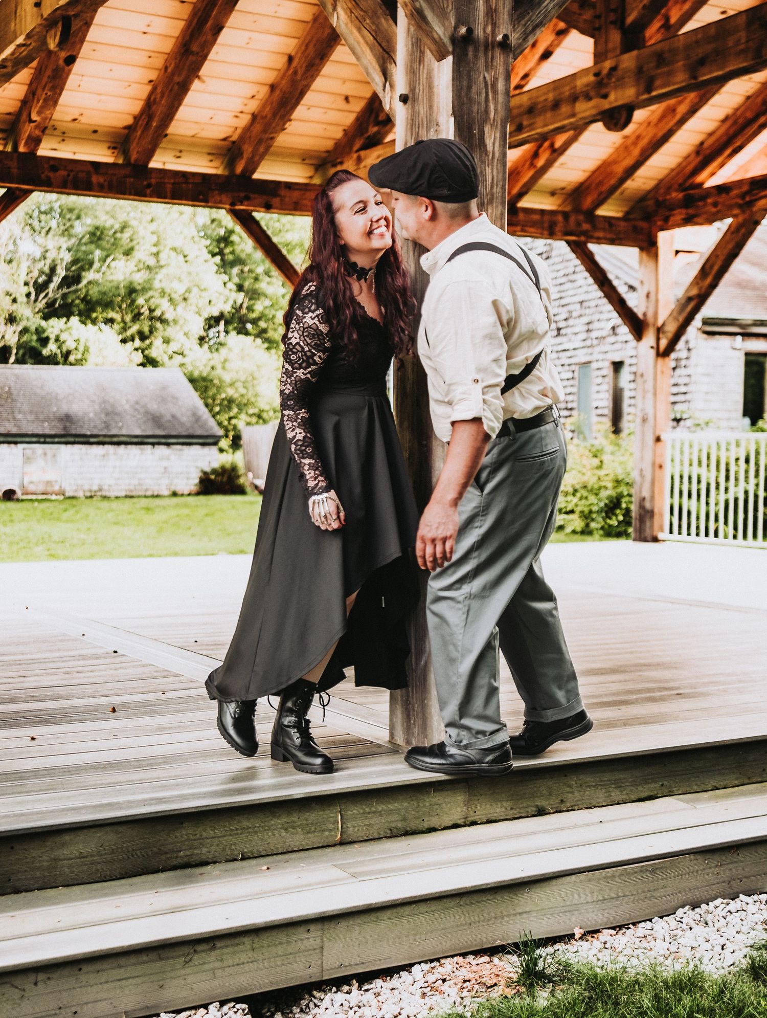 A couple in vintage style clothing dancing together under a rustic wooden pavilion on a sunny day for their engagement photos.