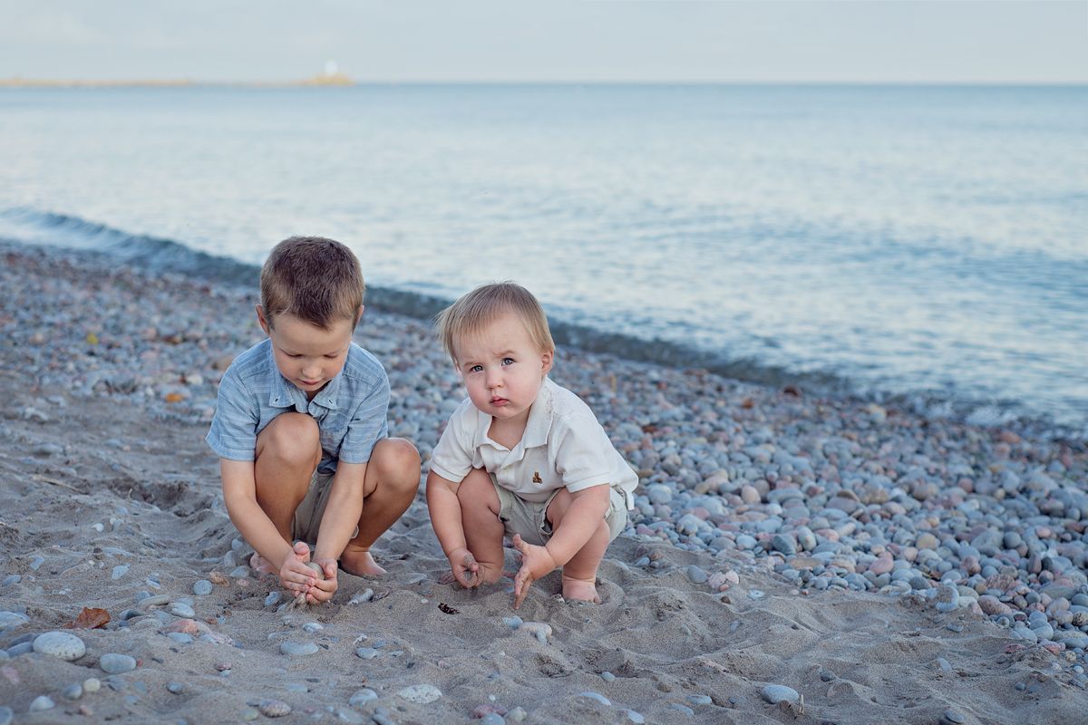 2 young boys in coordinated outfits play with the rocks at Bowmanville beach for a family photography session.
