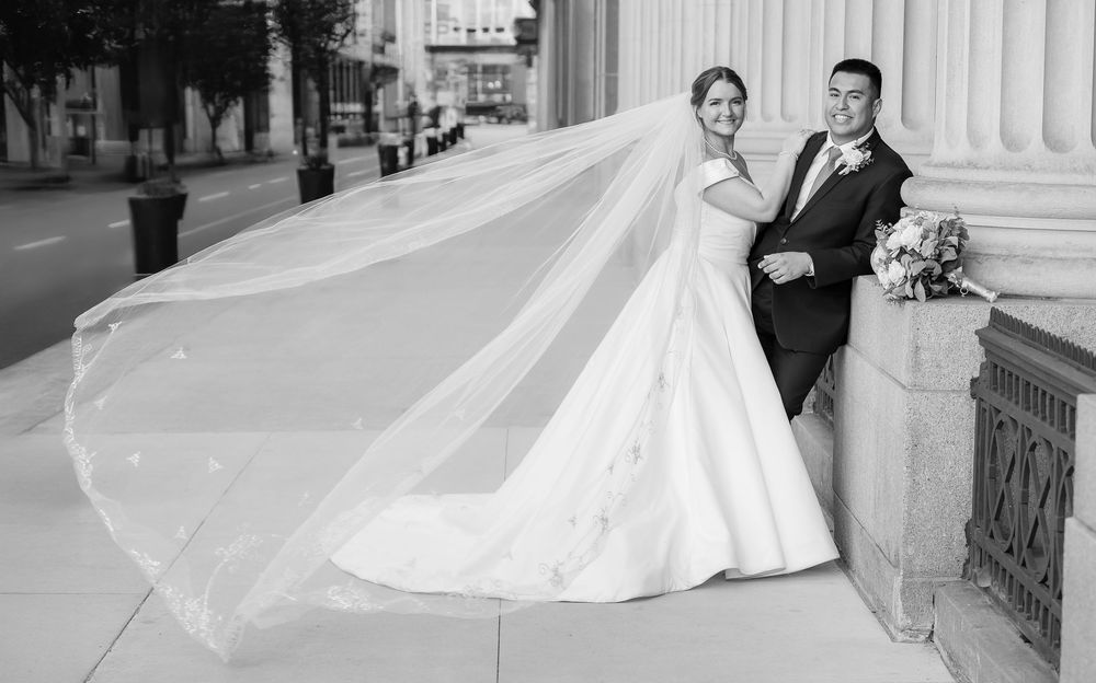 A wedding couple poses on marble steps in formal attire with a flowing white dress and classic tuxedo.