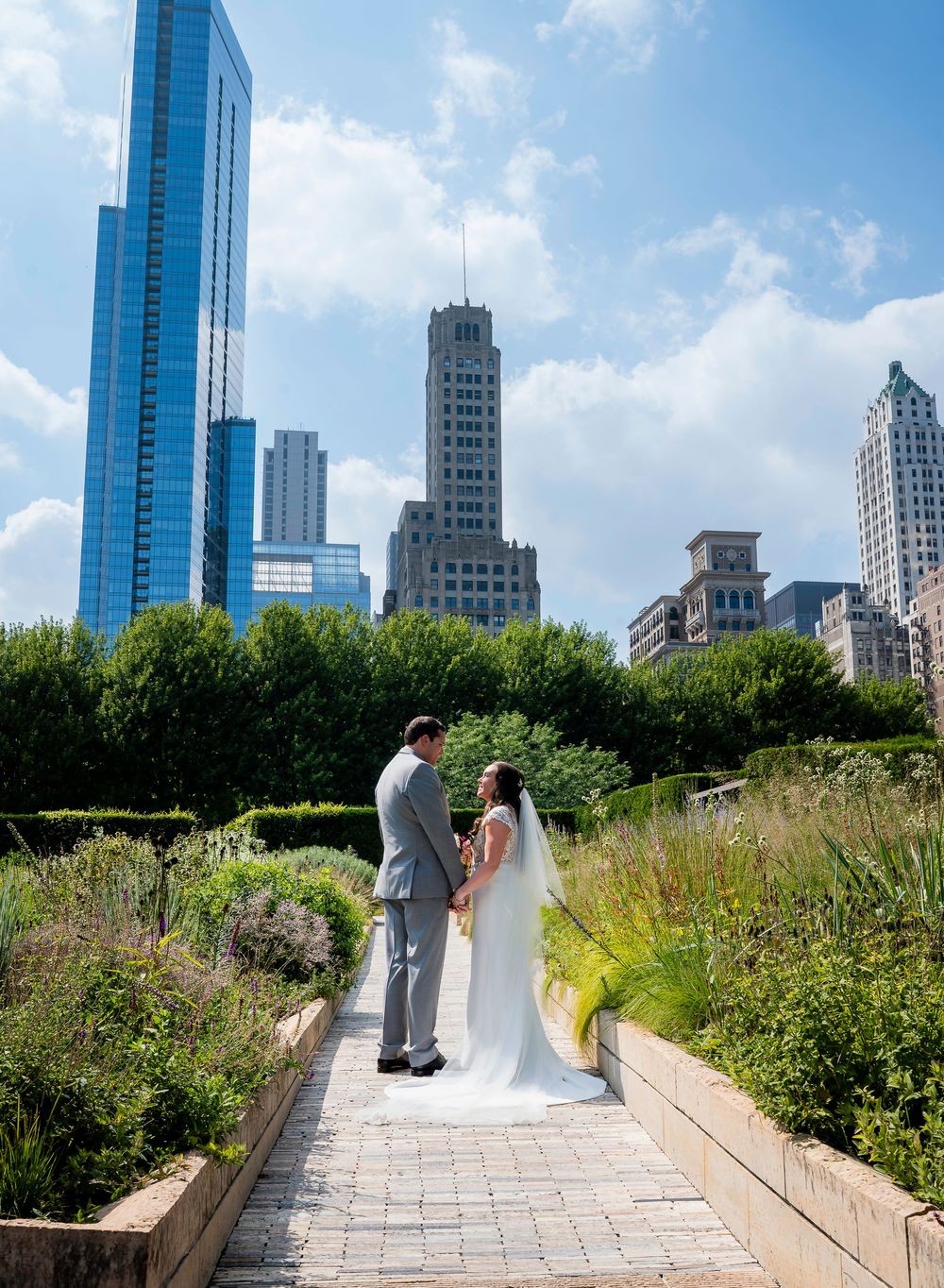 A wedding couple stands on a scenic rooftop garden path with Chicago skyscrapers rising in the background.