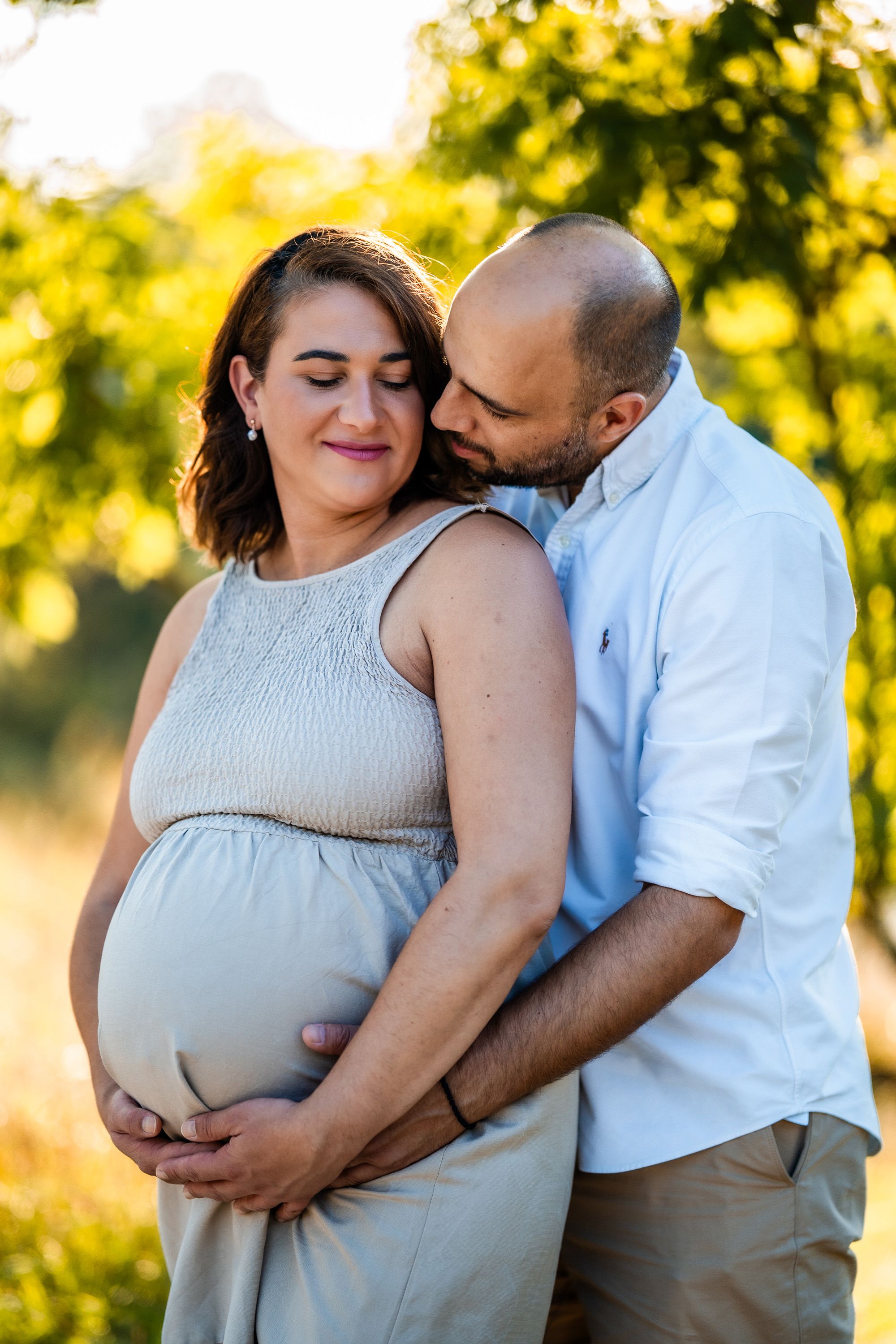 Tender maternity portrait of couple embracing in warm evening sunlight.