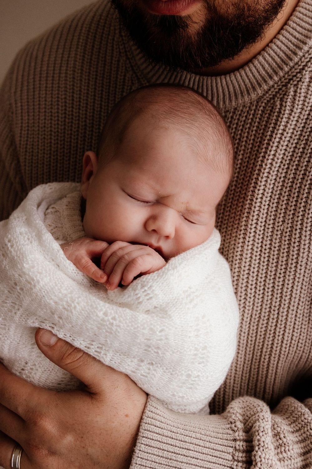 Close-up shots of baby wrapped in white blanket being held against beige knit sweater in a natural light studio in the blue mountains Sydney
