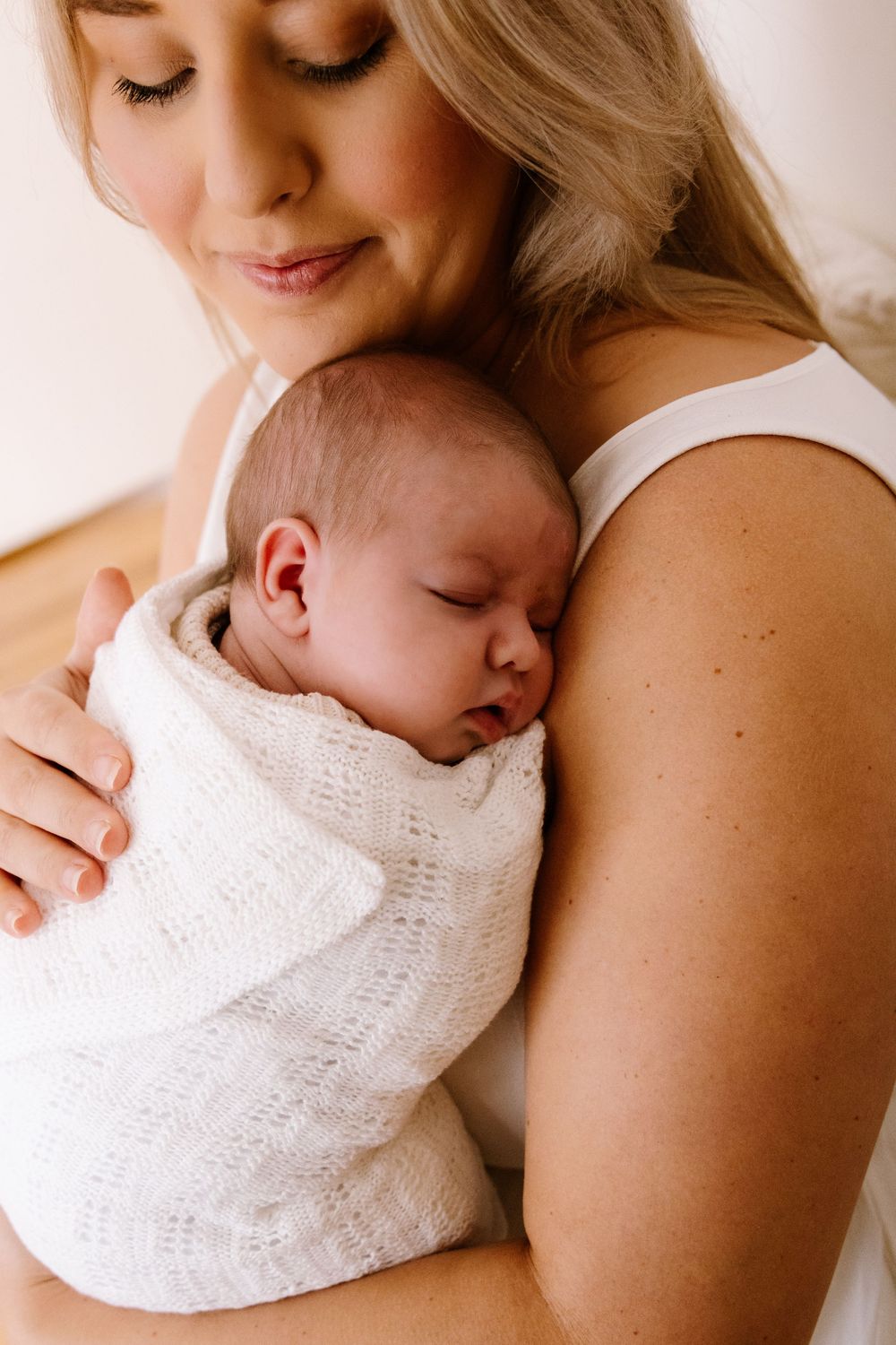 Tender moment between parent and sleeping newborn in white knit blanket. Captured in a natural light studio in the blue mountains Sydney