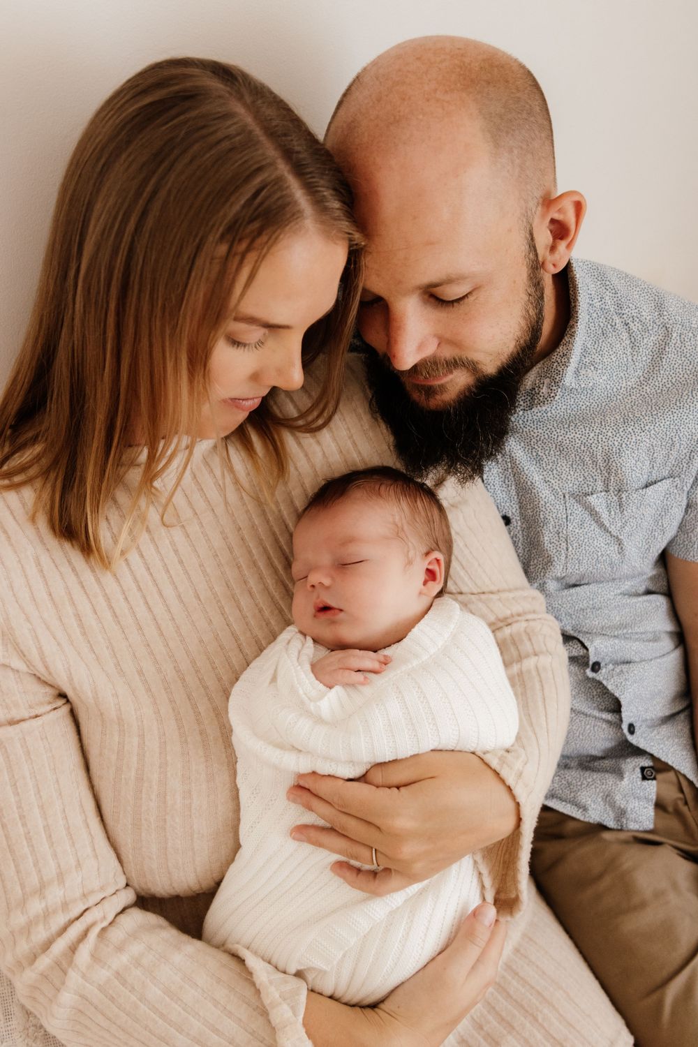 Family portrait series showing parents cuddling with their newborn baby against a light background.