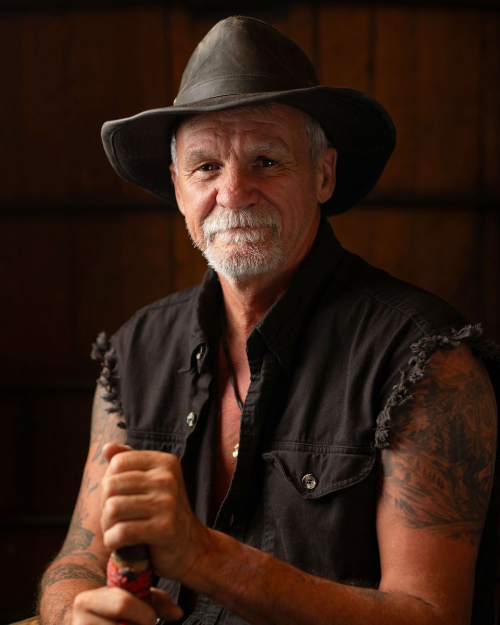 Older man with grey beard wearing wide-brim hat and black denim vest, holding walking stick - Okanagan portrait by Tania Veitch.