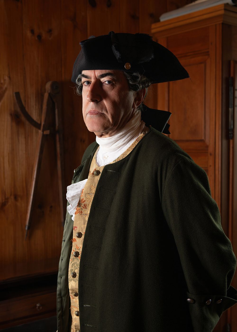 Environmental portrait of man in 18th century historical costume inside wooden heritage building.