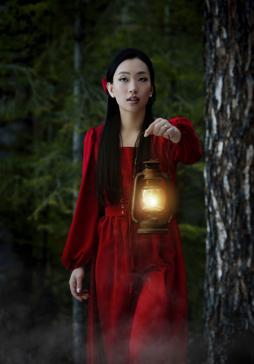 Cinematic portrait of woman in red dress holding lantern in forest at dusk.