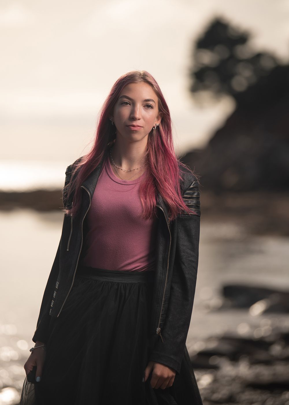 Teen girl with long pink hair in black jacket and tulle skirt posing by ocean  - Okanagan portrait photography by Tania Veitch.