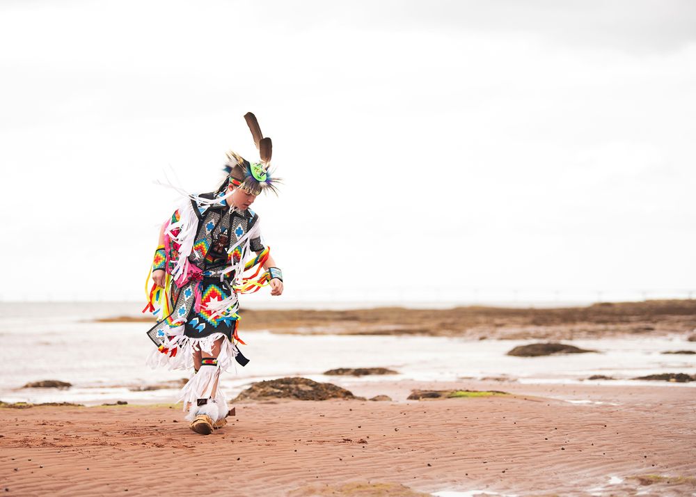Teenage boy in full regalia dancing on beach in Prince Edward Island - Okanagan portrait and cultural photography by Tania Veitch.