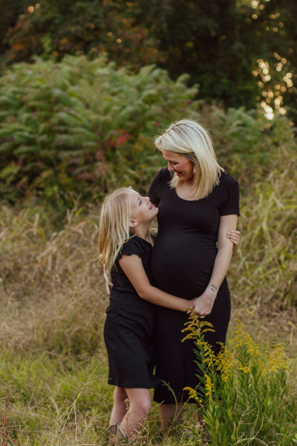A pregnant mother and her young daughter wearing matching black dresses on a fall day in Manila, Arkansas, by Delta Blossoms Photography