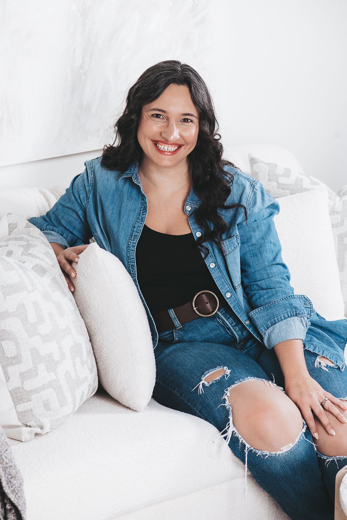 Jess Hammett, family photographer sitting on a white couch in denim, smiling