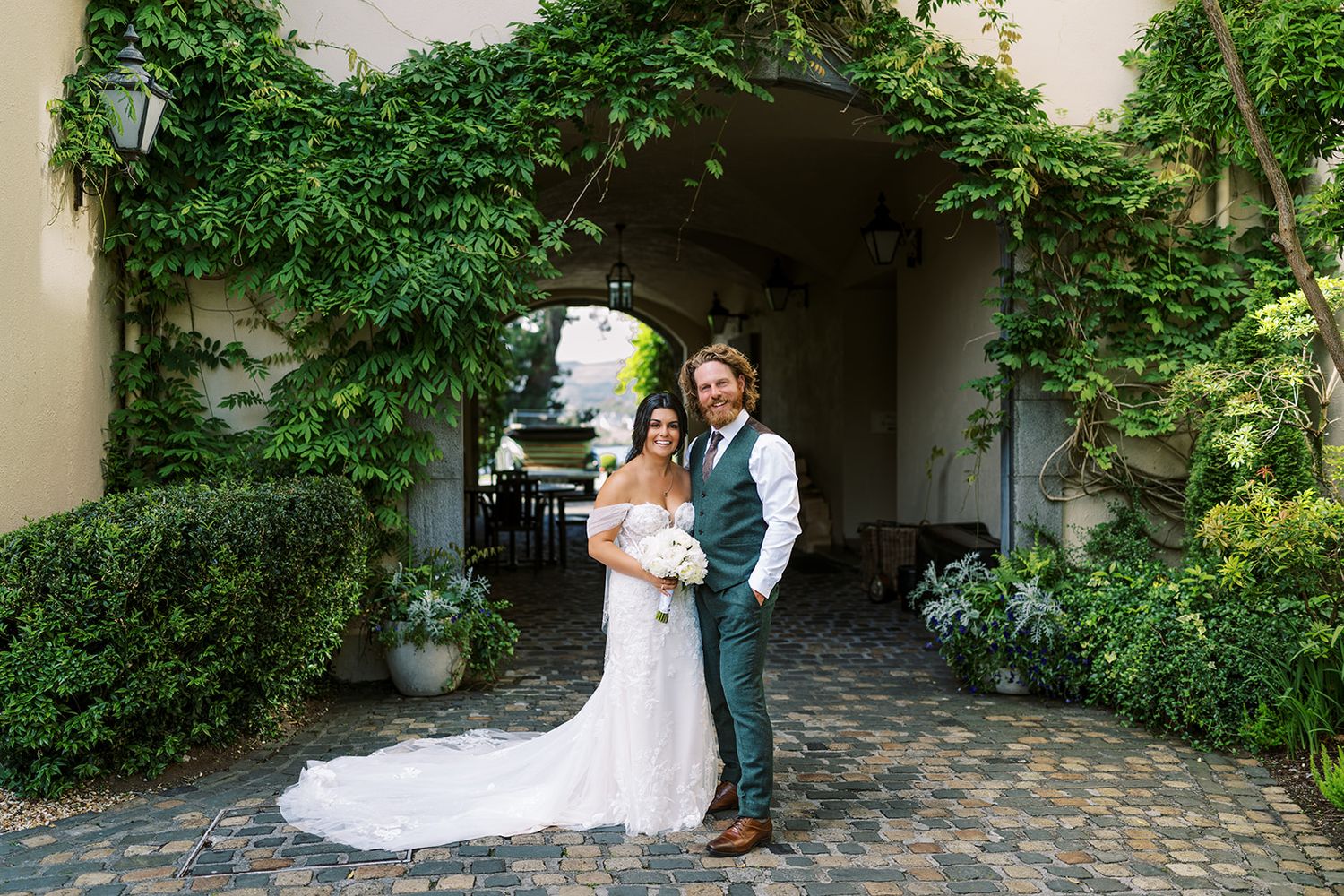 Wedding couple posing in romantic garden archway with vintage decor.