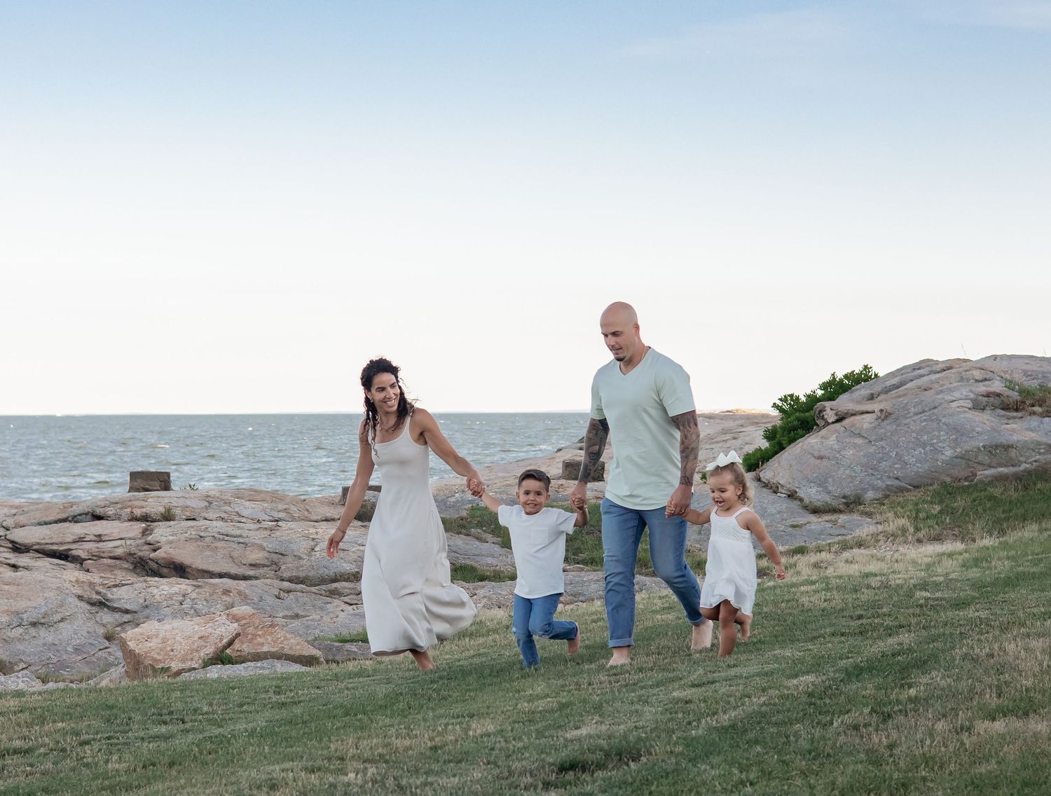 Family holding hands and walking together along coastal rocks at sunset.