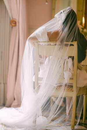 Flowing white wedding veil draped over vintage chair in soft natural light.