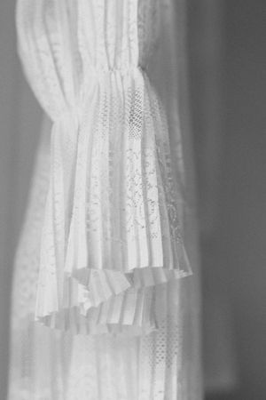 Black and white close-up of delicate white lace wedding dress details with pleated fabric.