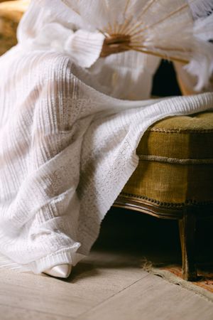 Detail shot of white wedding dress fabric draped over a vintage chair.