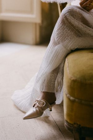 Elegant pointed shoes peeking out from under white lace fabric near a velvet chair.