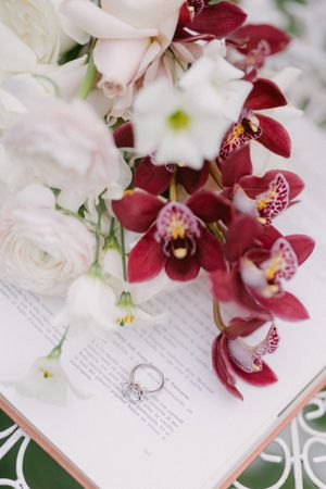 Wedding ring among red orchids and white roses on open book pages.