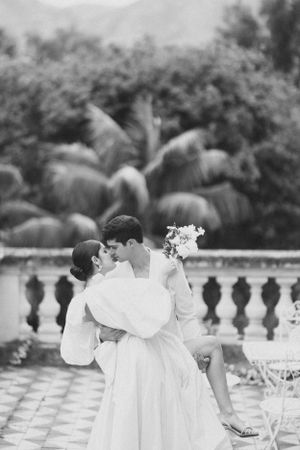 A romantic black and white photograph capturing an intimate moment on a terrace with decorative railings.