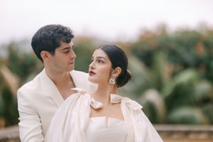 Romantic portrait of couple in white formal attire against greenery.