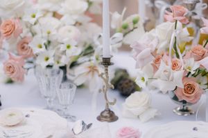 Elegant wedding table setting with pink roses, white flowers, and crystal glassware.