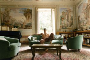 Luxurious vintage living room with ornate wall murals, green velvet furniture, and natural lighting.