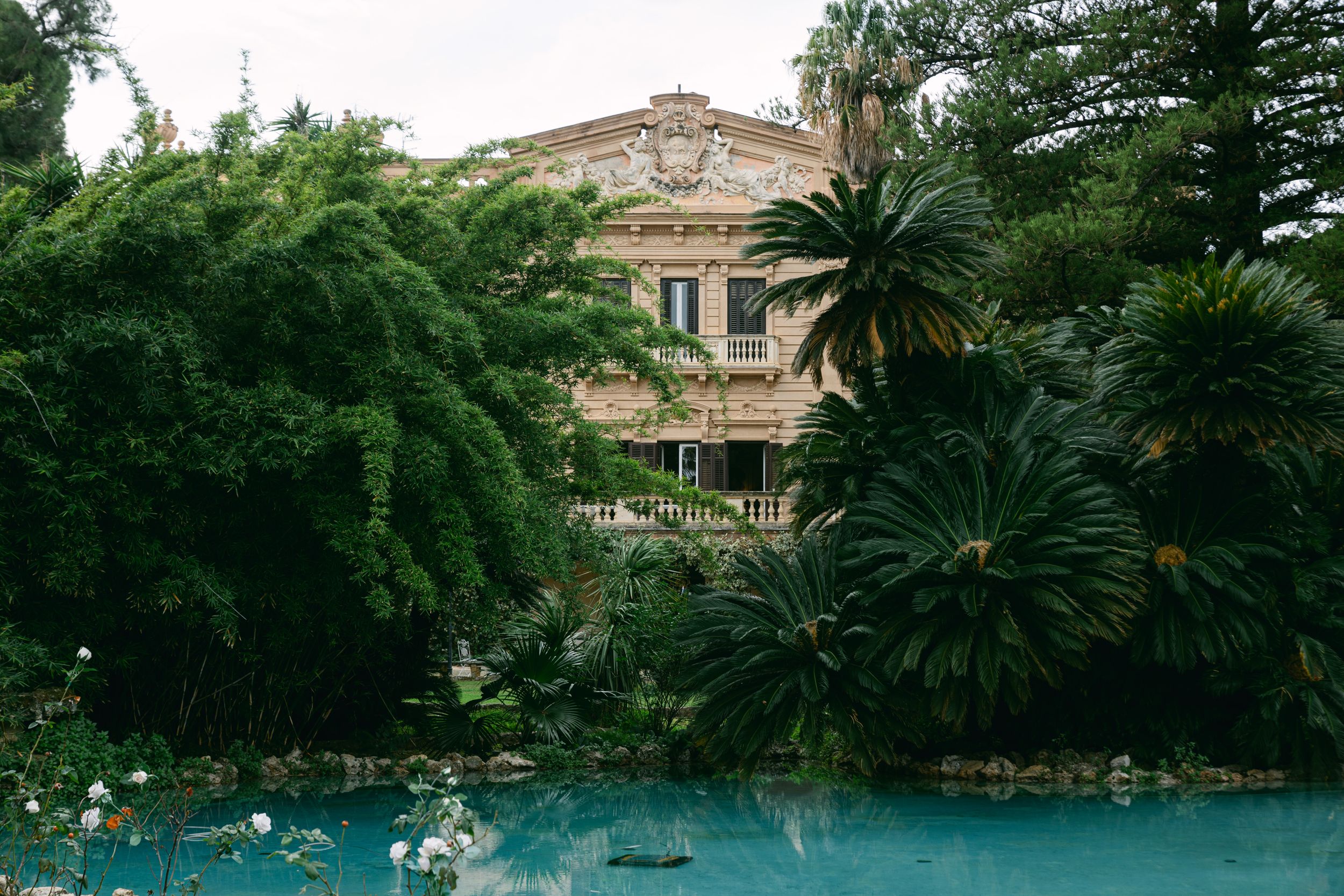 Historic villa with lush tropical gardens and turquoise pool surrounded by palm trees.