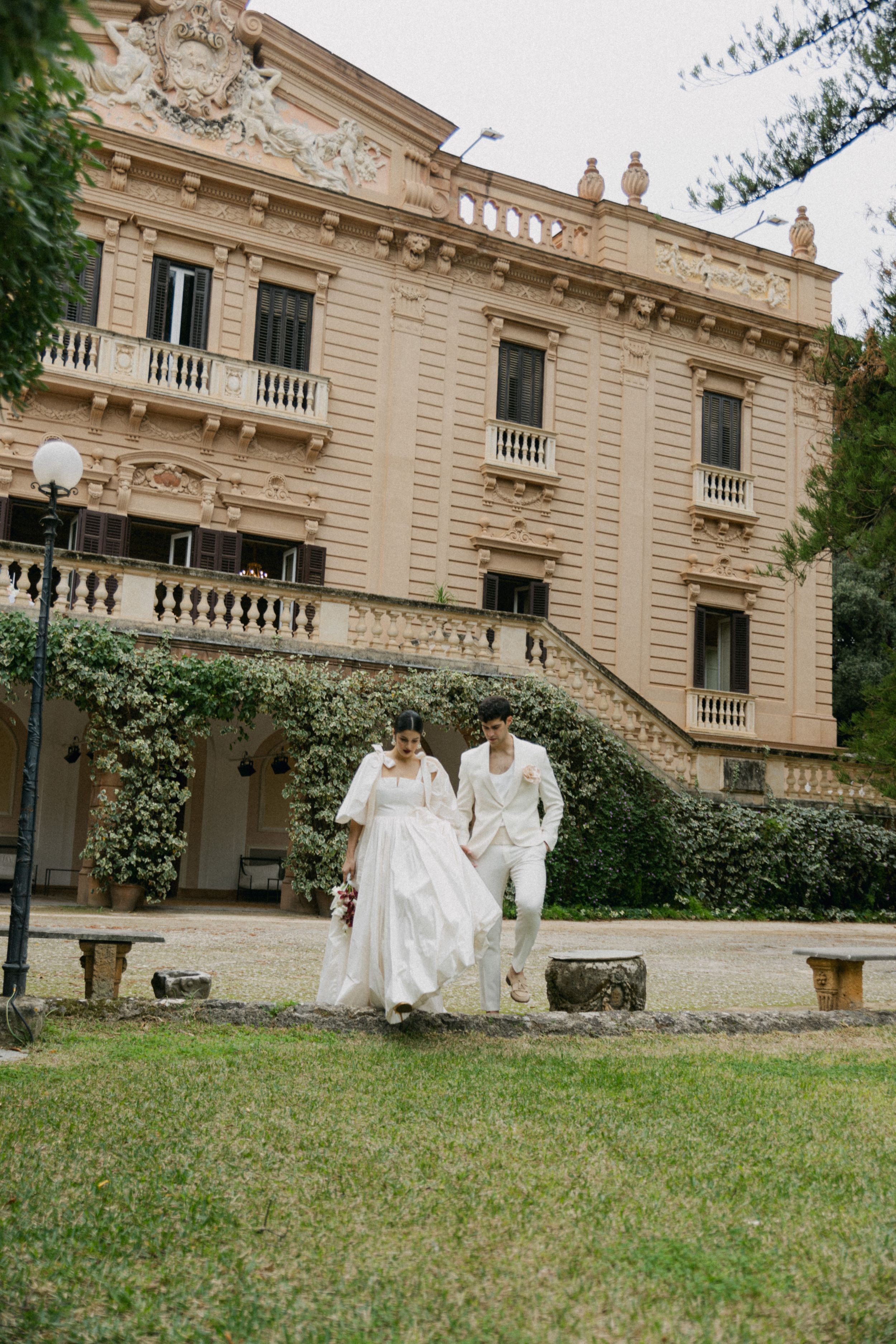 Couple descends stairs at grand historic mansion during wedding celebration.