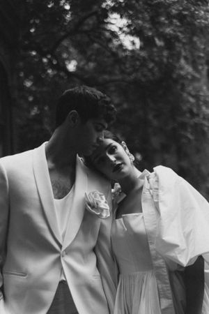 A romantic black and white portrait of a couple in white attire against a blurred natural backdrop.