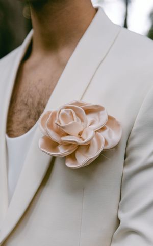 Elegant blush pink fabric flower boutonniere pinned to a white suit lapel.