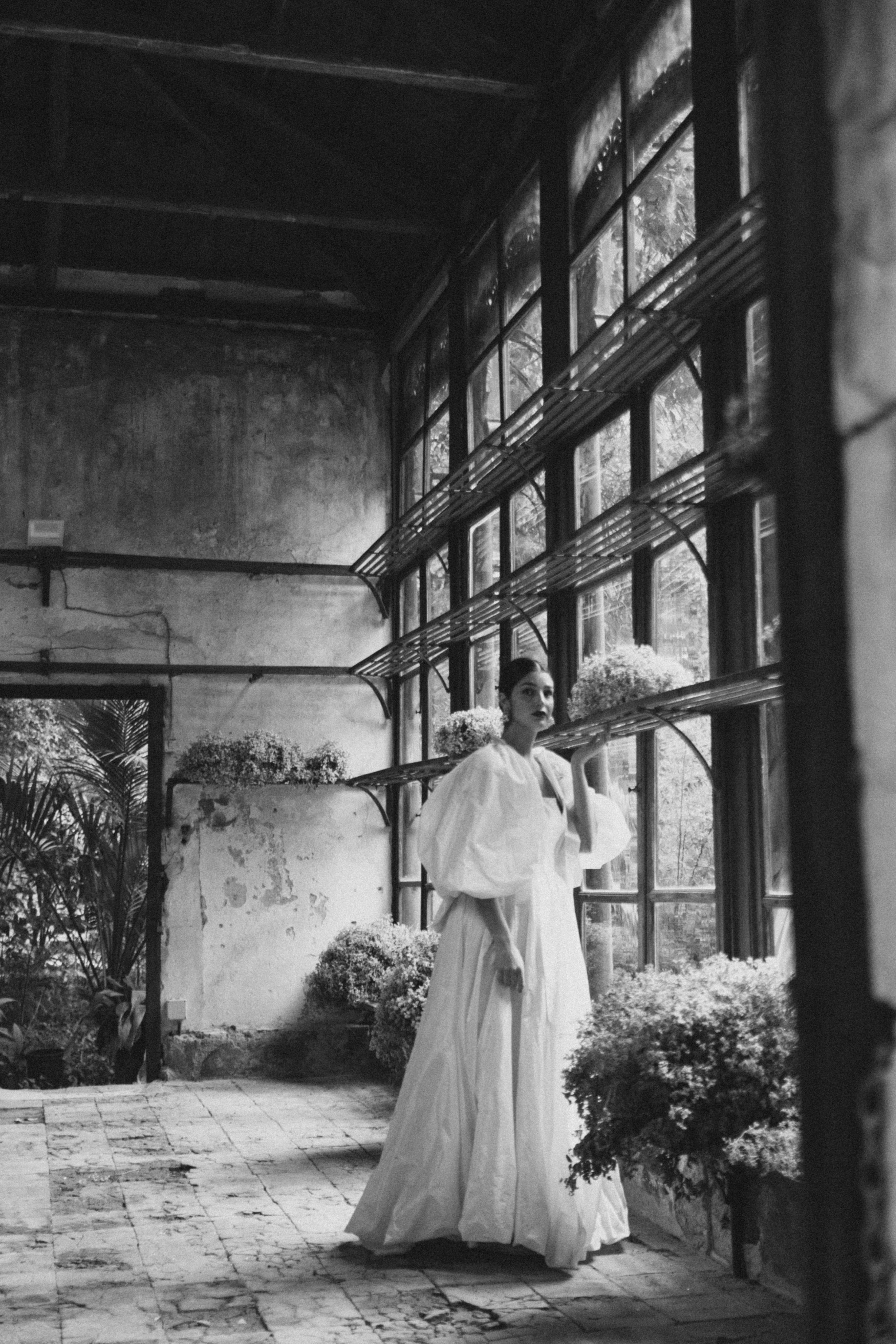 A vintage black and white photo showing a white dress in a sunlit conservatory space with window panes.