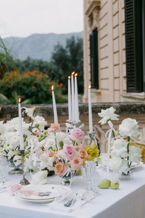 An elegant table setting with white and pink flowers, candles, and fine china against a mountain backdrop.