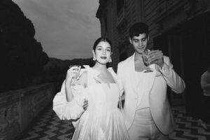 A black and white photo of a couple in elegant white attire enjoying drinks on a terrace.