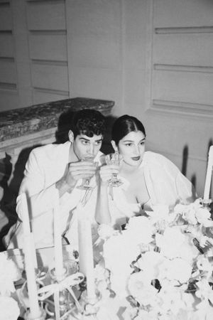 A black and white wedding reception photo with couple enjoying drinks among floral decorations.